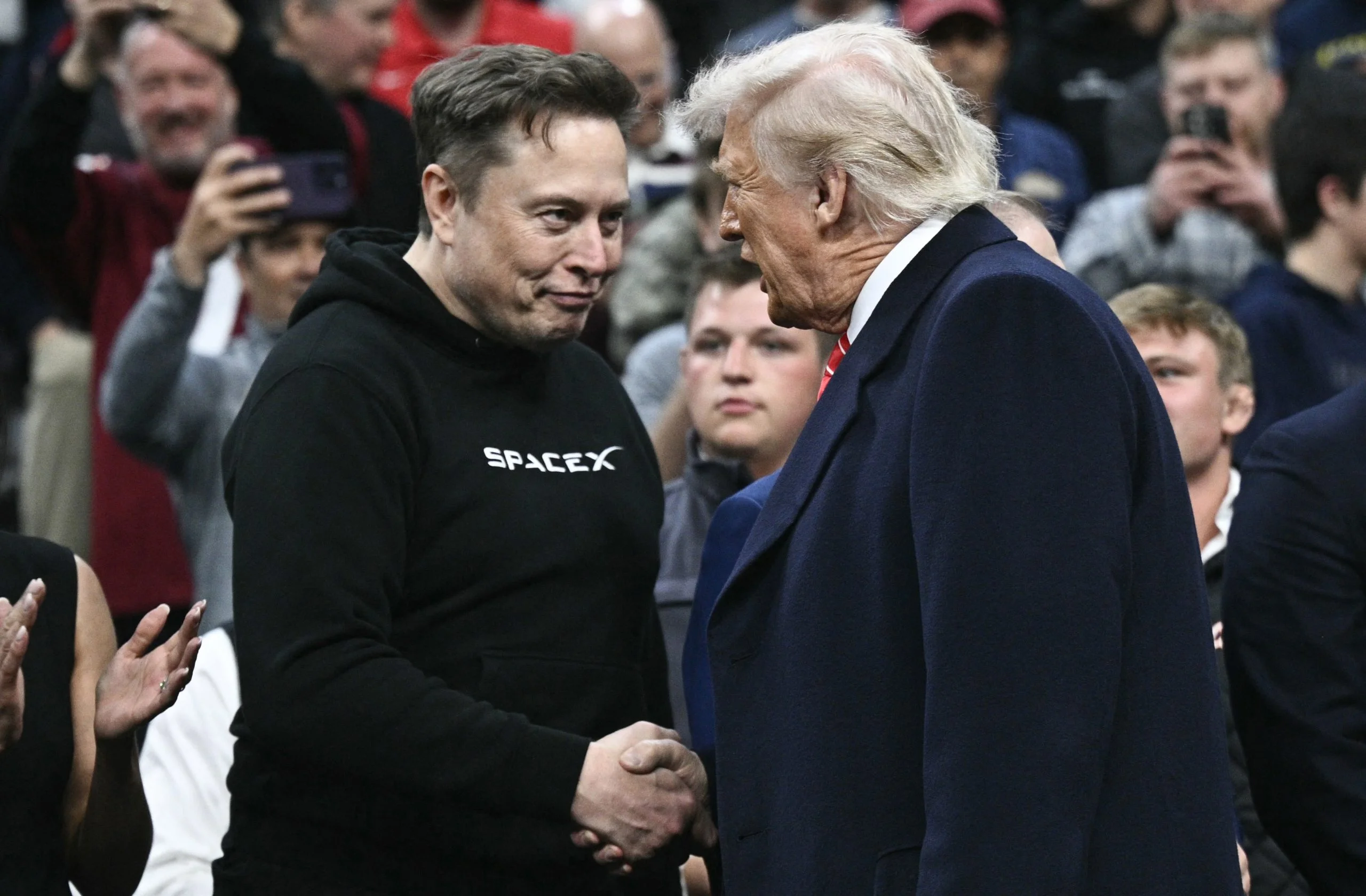 TOPSHOT - Tesla and SPaceX CEO Elon Musk and US President Donald Trump shake hands as they attend the men's NCAA wrestling competition at the Wells Fargo Center in Philadelphia, Pennsylvania, on March 22, 2025. (Photo by Brendan SMIALOWSKI / AFP) / ALTERNATE CROP (Photo by BRENDAN SMIALOWSKI/AFP via Getty Images)